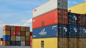 Vista aérea de varios contenedores marítimos apilados en un muelle portuario.