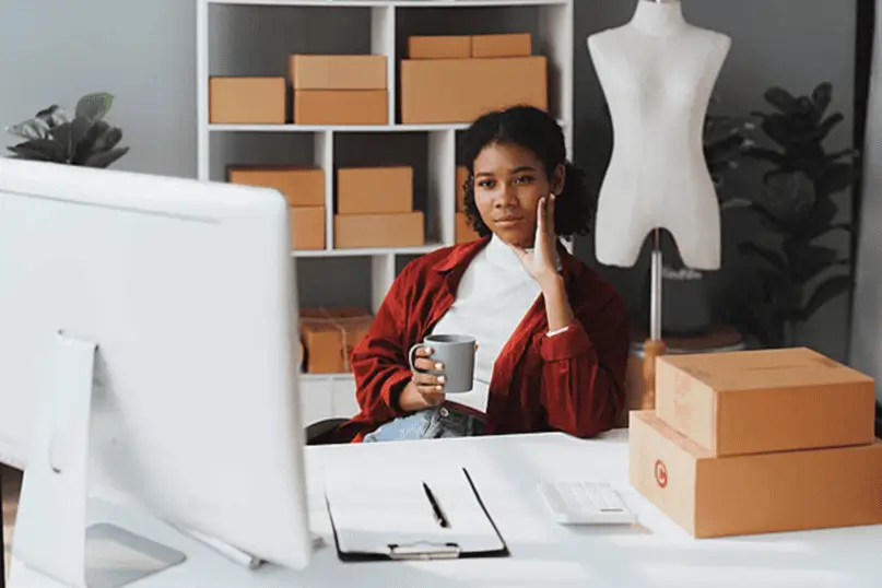 Emprendedora gestionando pedidos desde su escritorio rodeada de cajas, ejemplo práctico de cómo pequeñas empresas se benefician de qué es carga consolidada para optimizar costos de envío.